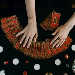 Hands arranging tarot cards on a table surrounded by candles and crystals, creating a mystical ambiance.